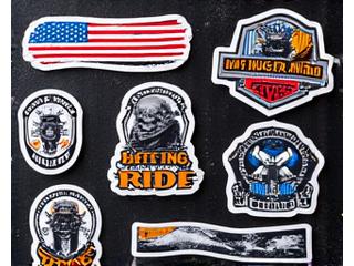 Collection of diverse motorcycle stickers including patriotic flags, vintage motorcycle designs, and abstract patterns